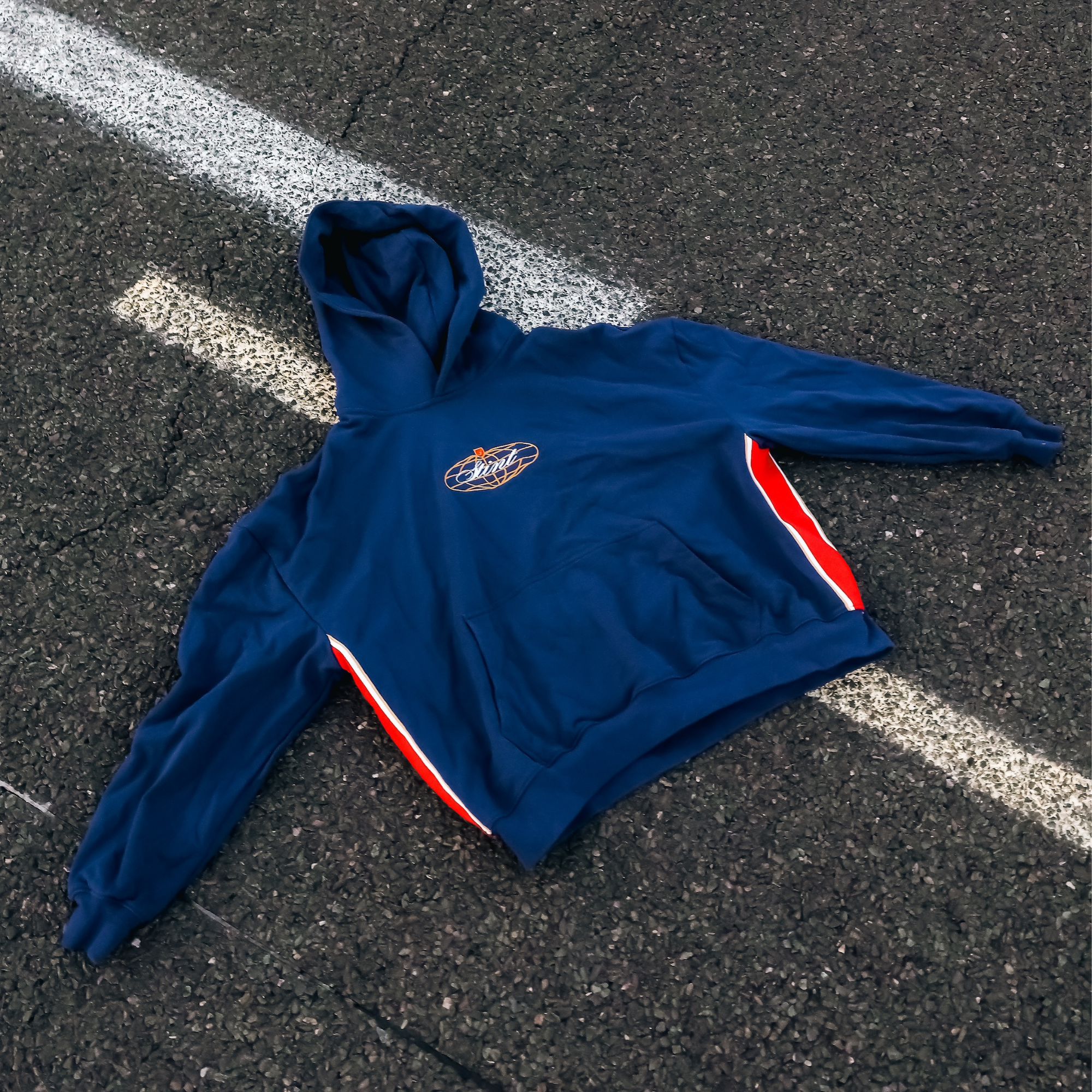 962 Hoodie by STINT GEAR. Blue, gold and red 956 and 962 livery on navy, laid on painted track asphalt. Motorsport livery apparel.